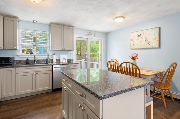 A kitchen with light blue walls, a granite countertop, wooden cabinets, a dining area with a table and chairs, and a 'BEACH' sign on the door.