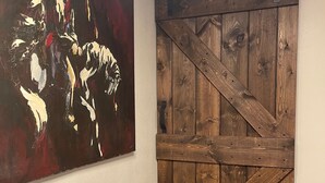 Een kamer met een houten schuifdeur in boerderijstijl en een groot abstract schilderij aan de muur.