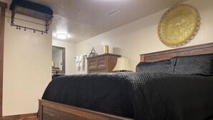 Een slaapkamer met een houten bed, nachtkastje, lamp, dressoir en een decoratief wandobject.
