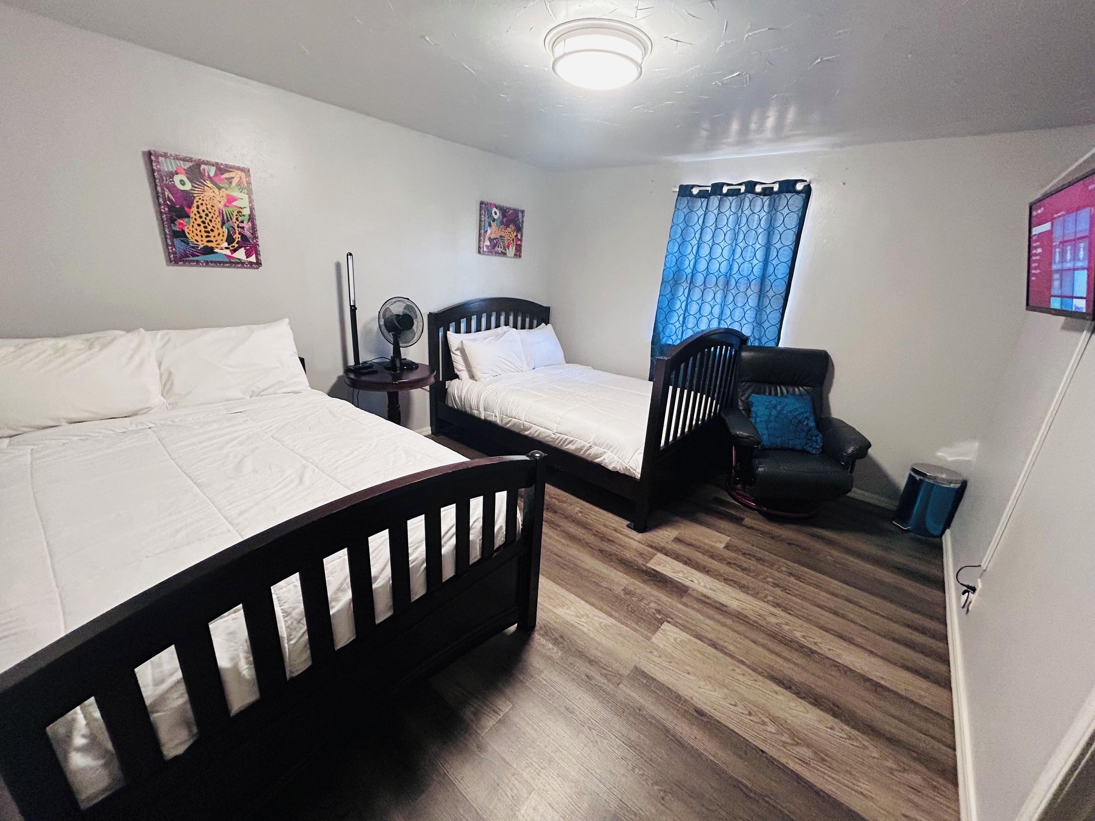 A bedroom with two beds, a chair, a fan, and artwork on the walls.