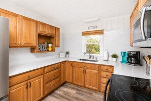 A kitchen with wooden cabinets, a stainless steel stove, a sink, and a window with a view of greenery.