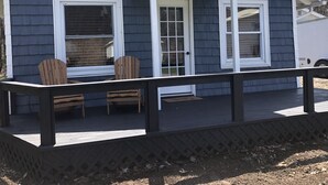 Een laag, eenverdiepings gebouw met een donkerblauwe gevel en witte details. Het heeft een overdekte veranda met twee houten stoelen en een bankje.