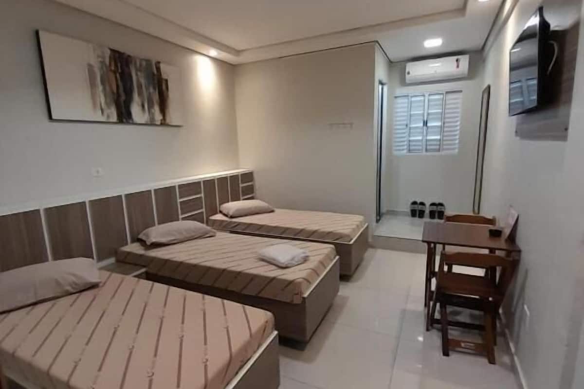 A hotel room with three single beds, a wooden desk, and a TV mounted on the wall.