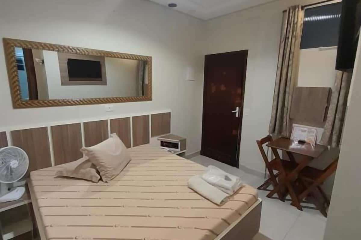 A hotel room with a large bed, a desk, a chair, a TV, and a mirror.