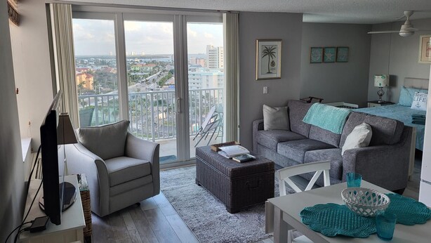 Un salon moderne avec un canapé gris, une petite table blanche et un balcon offrant une vue sur la ville.