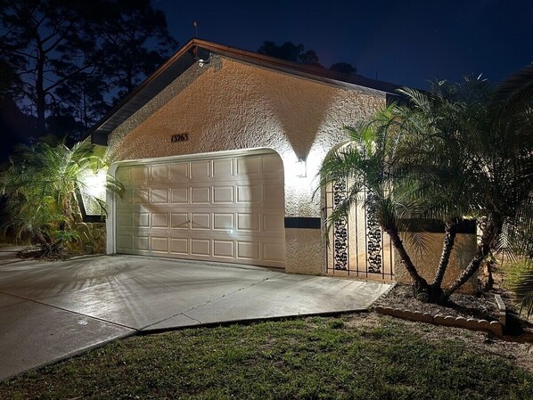 Eine Garage mit weißer Tür, Steinaußenwand und gut beleuchteter Auffahrt.