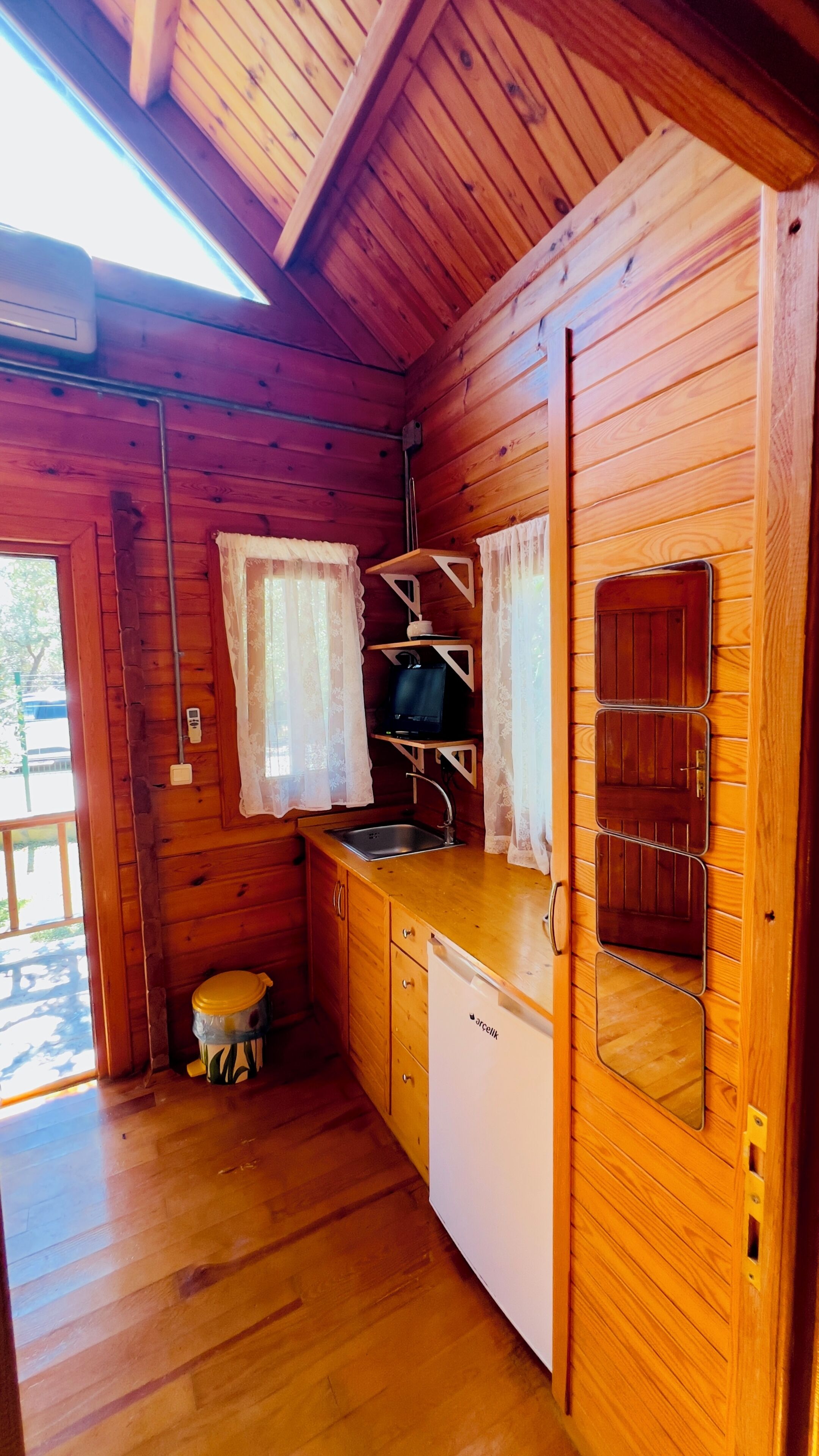 Une petite cabane en bois comprenant un coin cuisine équipé d’un évier, d’un petit réfrigérateur et d’une cuisinière.