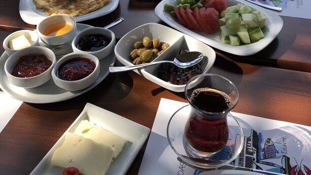 A table set with various dishes, including cheese, olives, and vegetables, with a view of the sea in the background. - Yelkovan Zeytin Evi (Marmara)