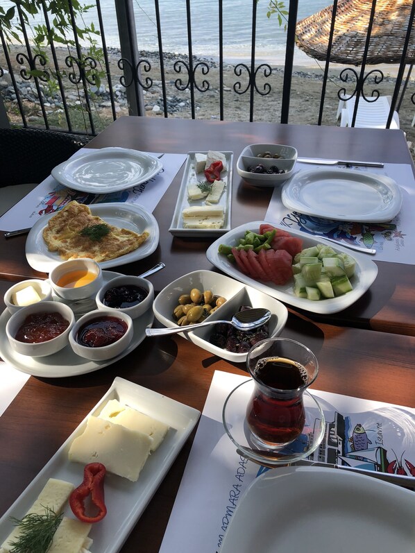 A table set with various dishes, including cheese, olives, and vegetables, with a view of the sea in the background. - Yelkovan Zeytin Evi (Marmara)