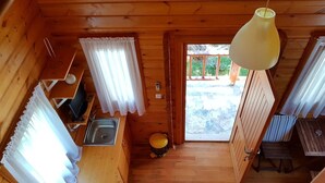 A cabin interior with a wooden floor, a kitchen area with a sink and cabinets, a yellow stool, and a door leading outside. - Yelkovan Zeytin Evi (Marmara)