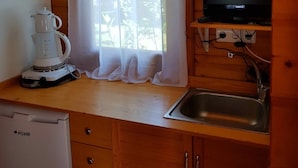 A compact kitchen with wooden cabinets, a white kettle, a small sink, and a television on a shelf. - Yelkovan Zeytin Evi (Marmara)
