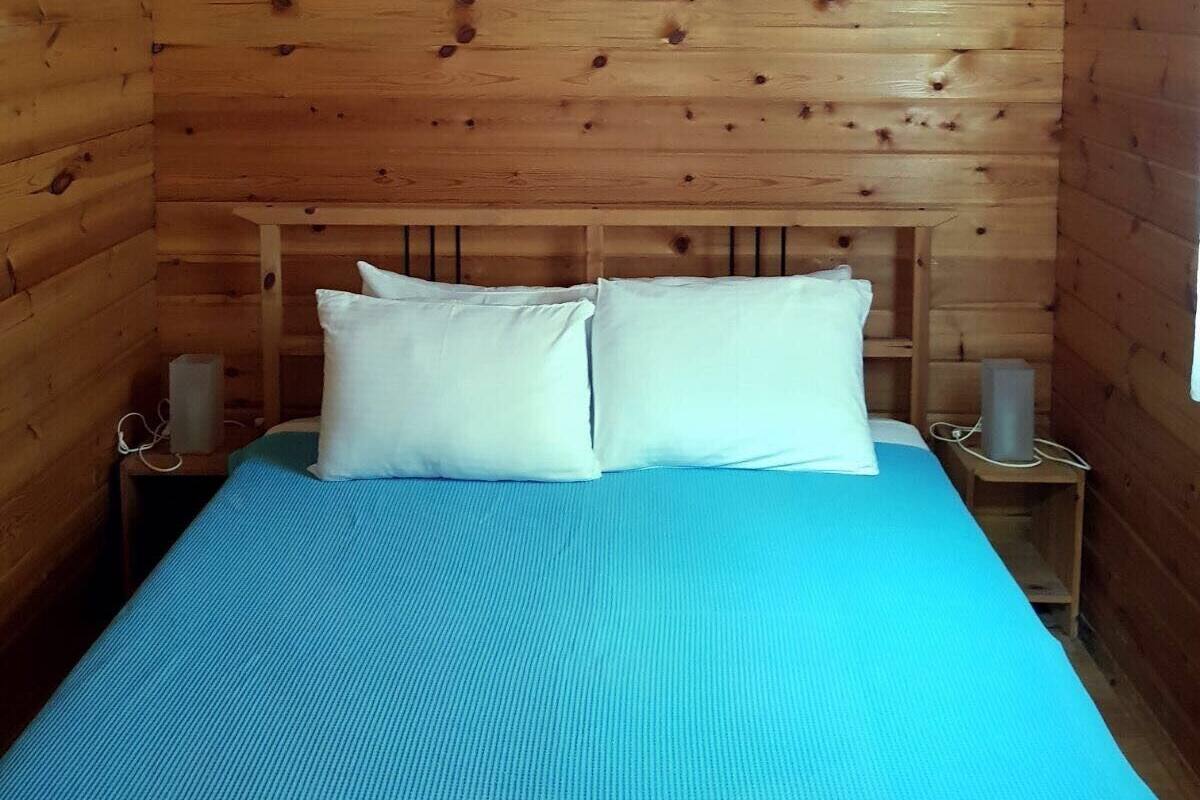 A wooden cabin room with a bed, two bedside tables, and a window.