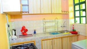 Una cucina con mobili bianchi, un piano cottura a gas, un lavandino e una finestra con stipiti verdi.