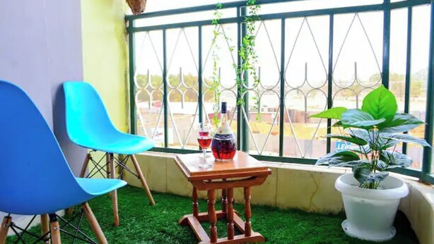 Un balcone con due sedie blu, un tavolino in legno con una bottiglia e un bicchiere, e una pianta in vaso.