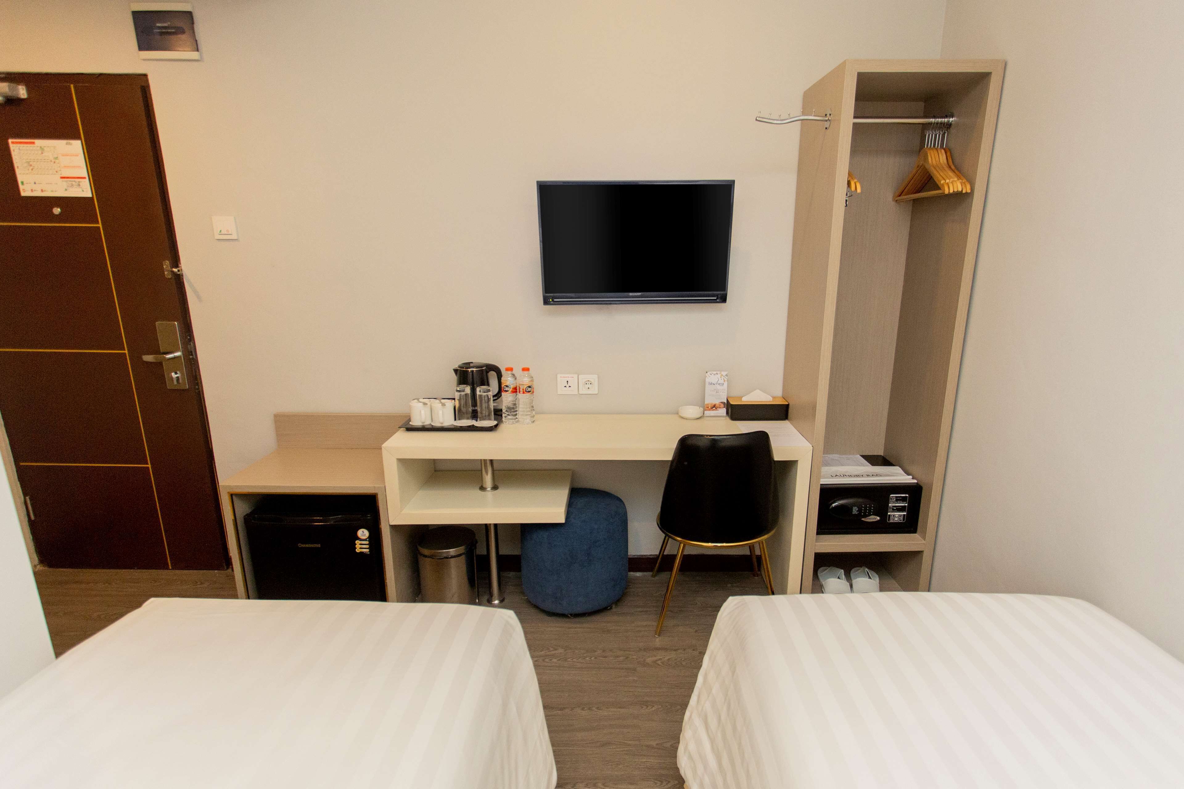 A hotel room with two beds, a desk with a flat-screen TV, a wardrobe, and a small kitchenette.