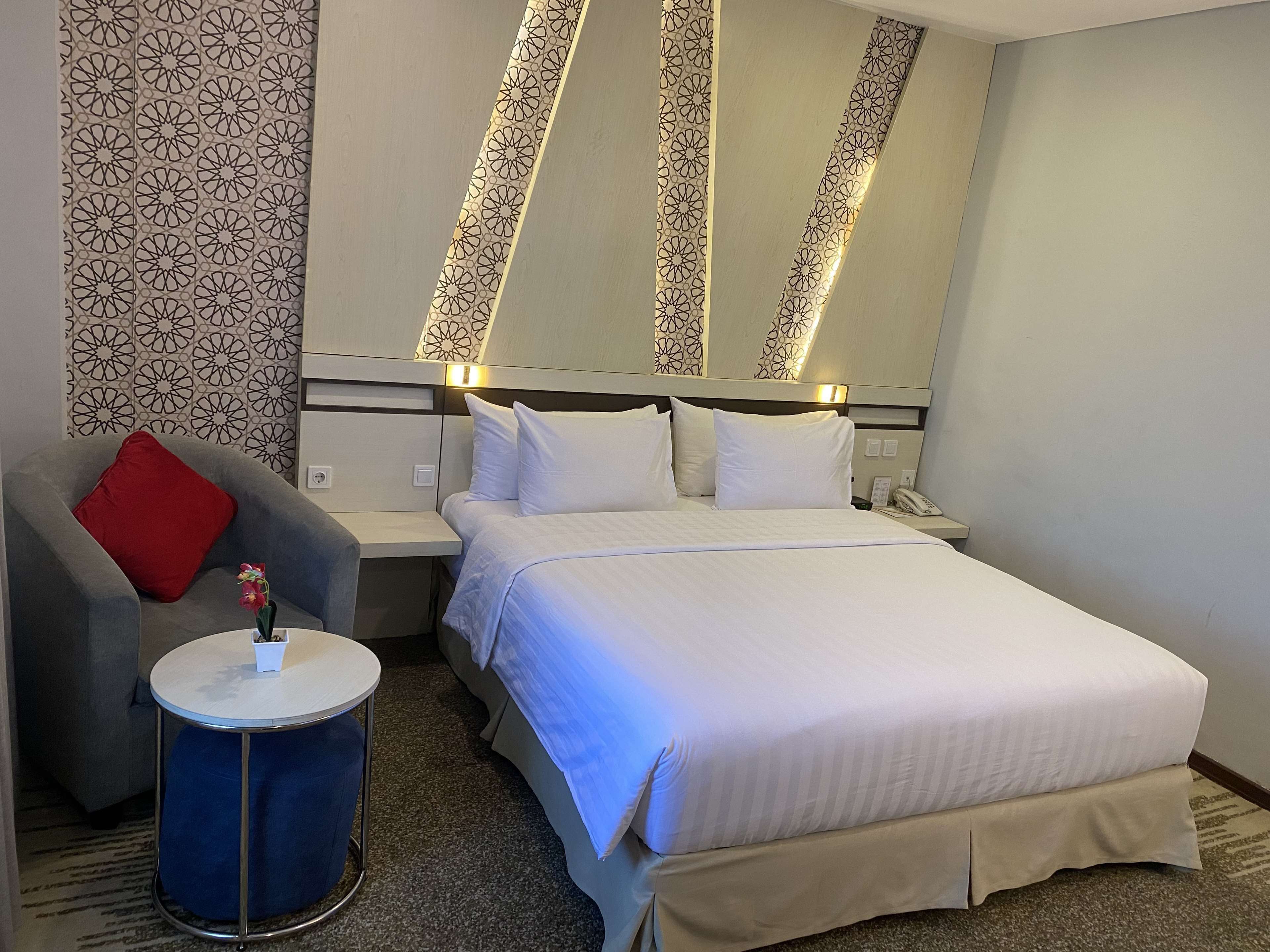 A hotel room with a bed, a nightstand, a chair, and a small table.