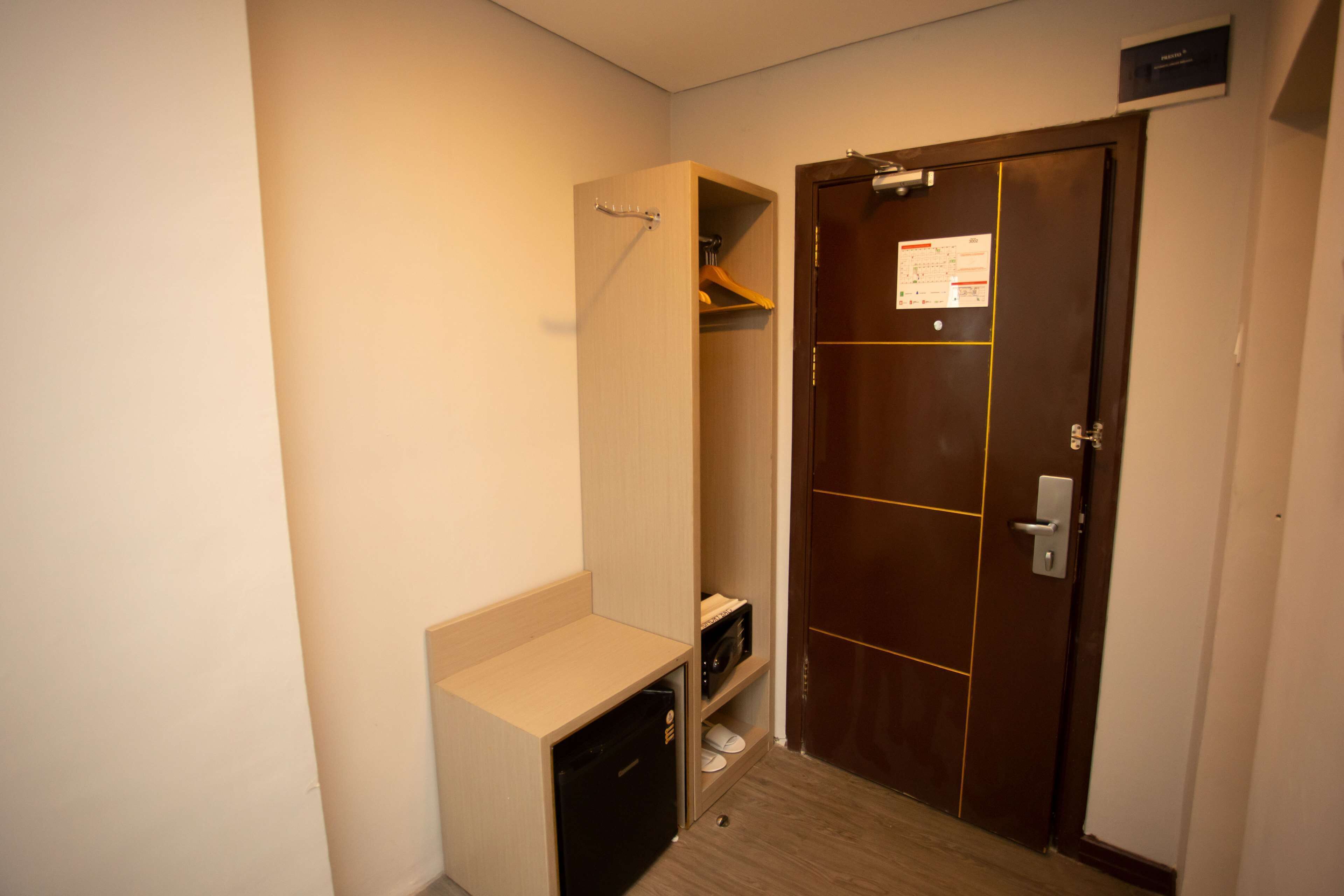 A compact hotel room with a wooden door, a small built-in closet, and a compact kitchenette area.
