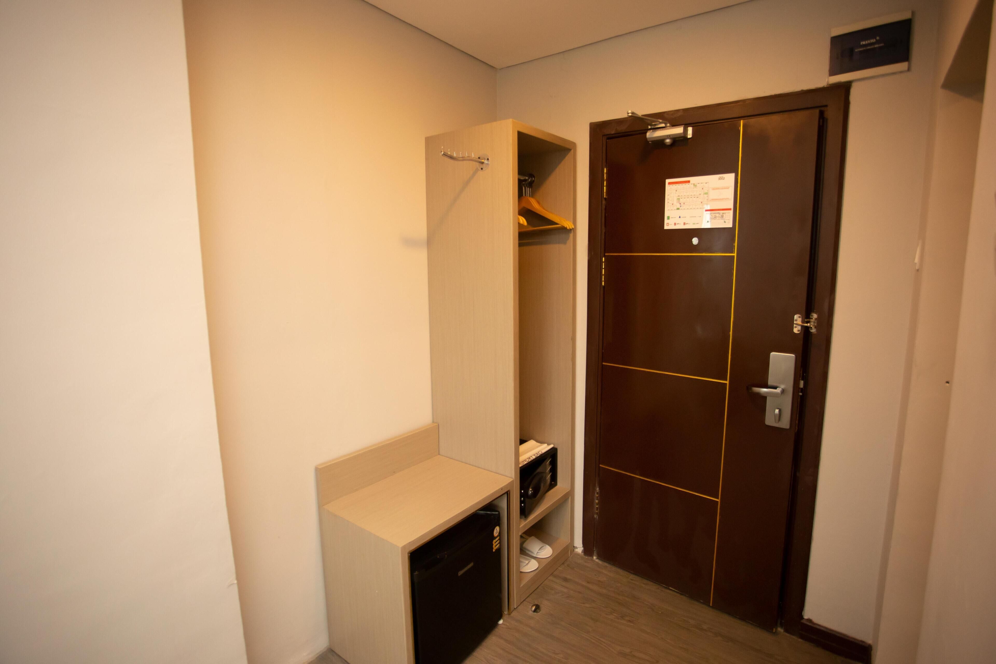 A compact hotel room with a wooden door, a small built-in closet, and a compact kitchenette.