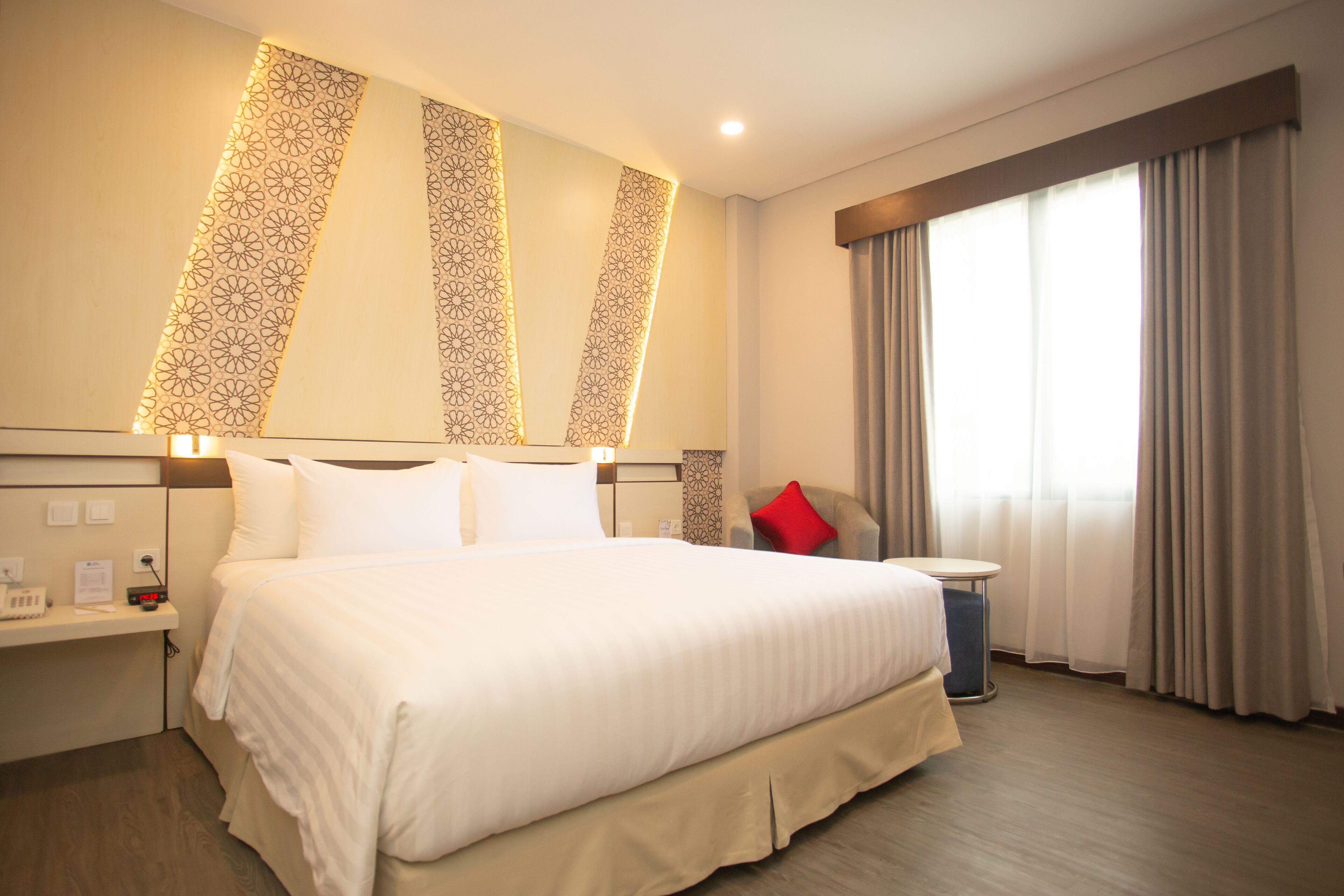 A hotel room with a large bed, bedside tables, a desk, and a window with curtains.