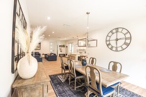 Een eetgedeelte met een houten tafel, stoelen en een grote wandklok.
