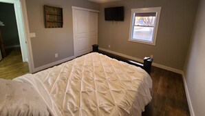 Un dormitorio con cama, ventilador de techo, televisor, ventana y puerta.