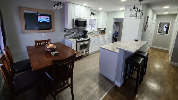 Una cocina moderna con armarios blancos, una isla central y una zona de comedor con mesa y sillas de madera.