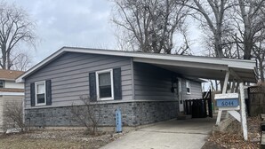 Una casa residencial con cimientos de piedra, fachada gris y un letrero con el número 6044.