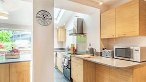 A modern kitchen with wooden cabinets, a built-in oven, a microwave, and a clock on the wall. - 4 bedroom accommodation in Keswick (Keswick)