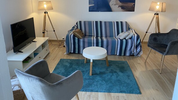 Ein Wohnzimmer mit einem gestreiften Sofa, einem Fernseher, zwei Lampen, einem runden Tisch und einem Bild von einer Strandlandschaft.