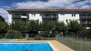 Ein Swimmingpool mit glasklarer, blauer Wasseroberfläche, umgeben von einem Metallzaun, im Hintergrund ein Gebäude mit Balkonen.