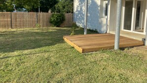 Ein Garten mit Holzterrasse, umzäuntem Bereich und einem Haus mit Schiebetür.