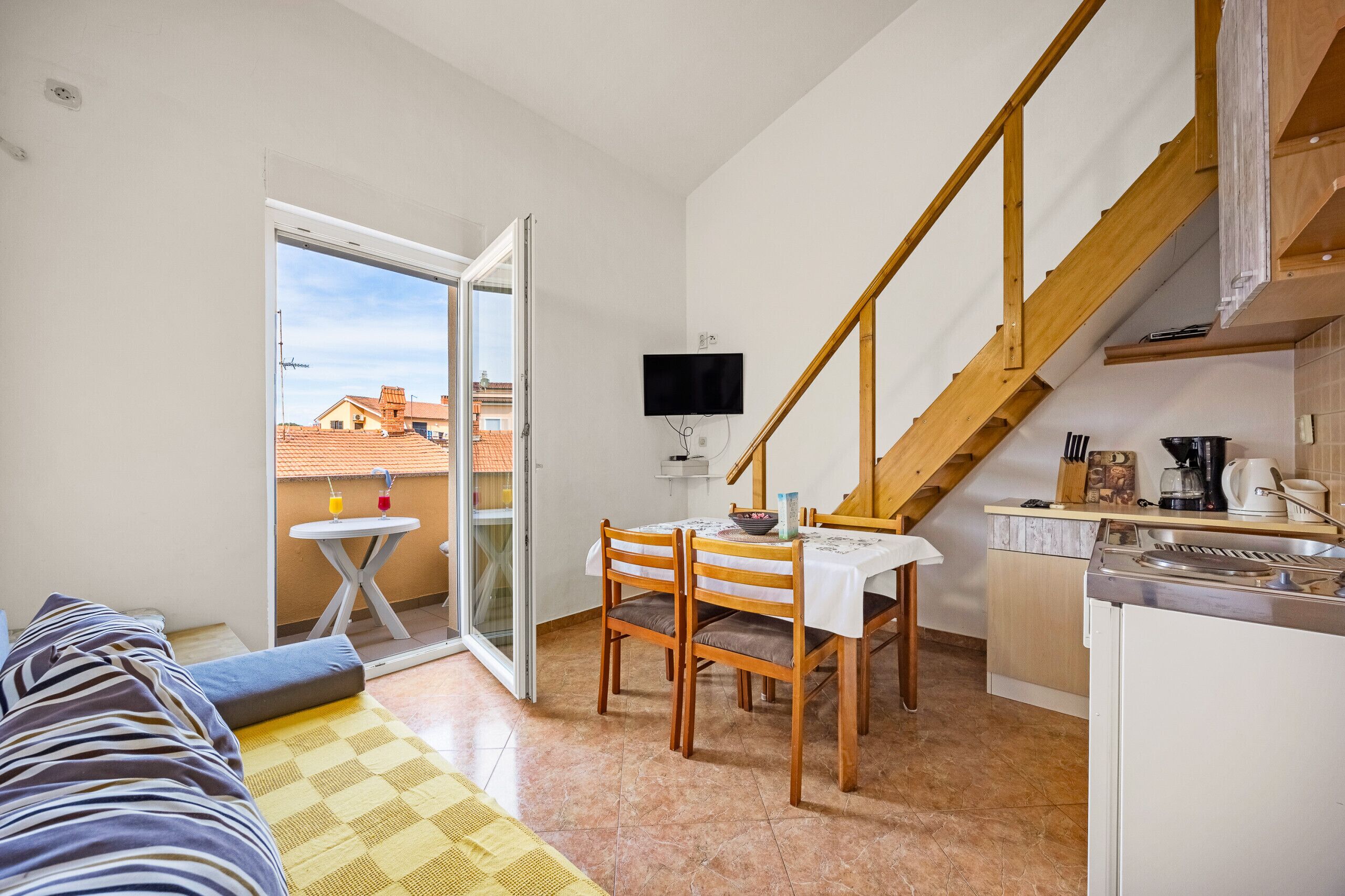 A compact living space with a dining area, kitchenette, and a balcony with a view of buildings.