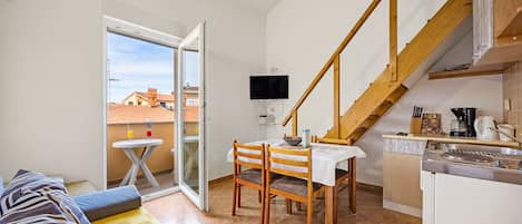 A compact living space with a dining area, kitchenette, and a balcony with a view of buildings.