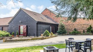 A rustic barn-style building with a red door, a paved patio with outdoor seating, and a brick wall in the background. - Cedar Barn - UKC5406 (Banham)