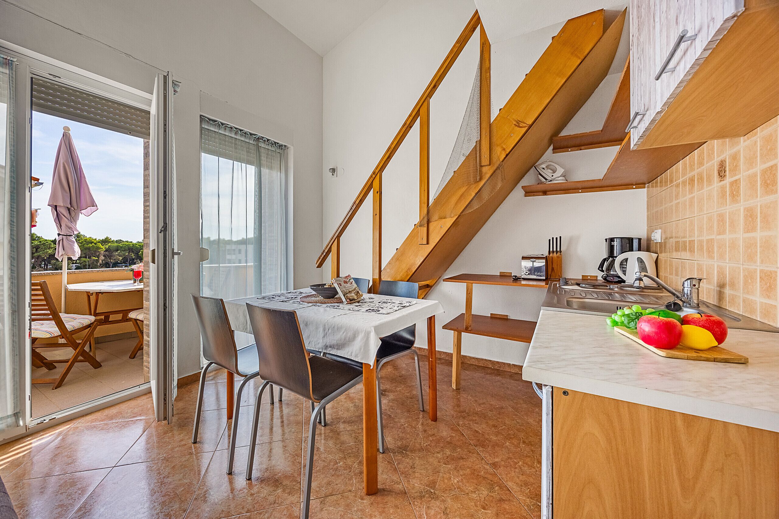 Uma área de refeições com mesa e cadeiras, uma cozinha com pia e bancada, e uma escada de madeira.