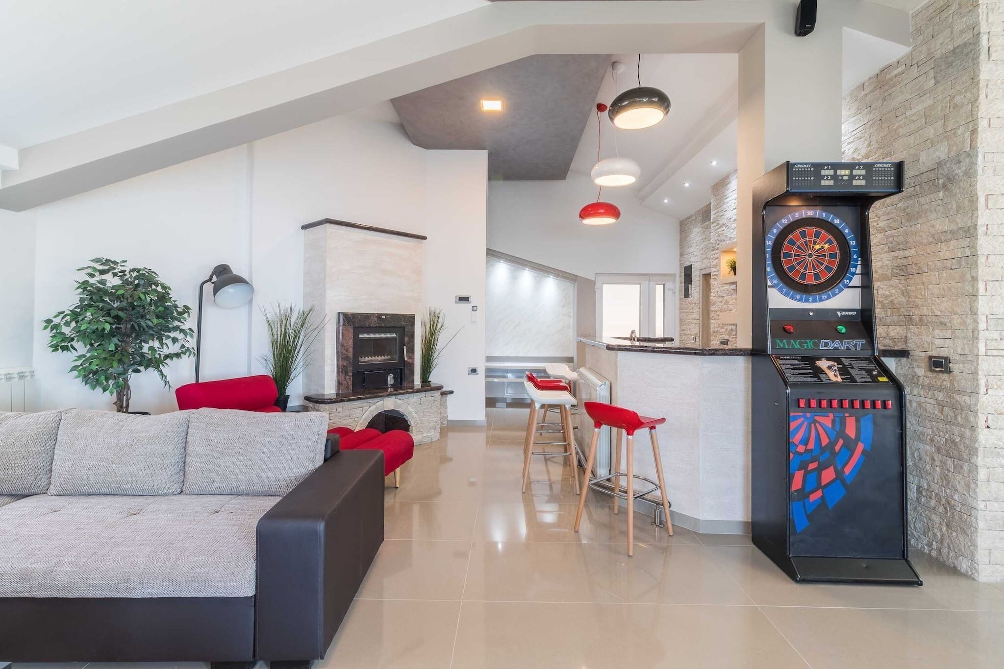 A modern living room with a sofa, red cushions, a fireplace, and a dartboard.