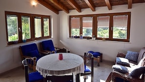 A room with a wooden ceiling, a round table with a white tablecloth, blue chairs, and a sofa with blue cushions.