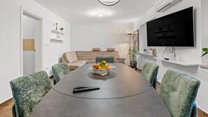 A modern dining area with a large table, green upholstered chairs, a fruit bowl, and a remote control on the table. - Apartment Pineta close to the Beach (Medulin)
