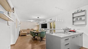 A modern kitchen with a central island, a dining area with green chairs, and a living room with a sofa and a TV. - Apartment Pineta close to the Beach (Medulin)