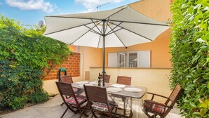 A patio with a table and chairs under a large umbrella, surrounded by greenery and a brick wall. - Charming Pool Apartment Liznjan - Buneta (Ližnjan)