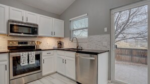 A modern kitchen with white cabinets, stainless steel appliances, and a large window overlooking a fenced yard.