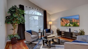 A modern living room with a large window, a painting, and a potted plant.