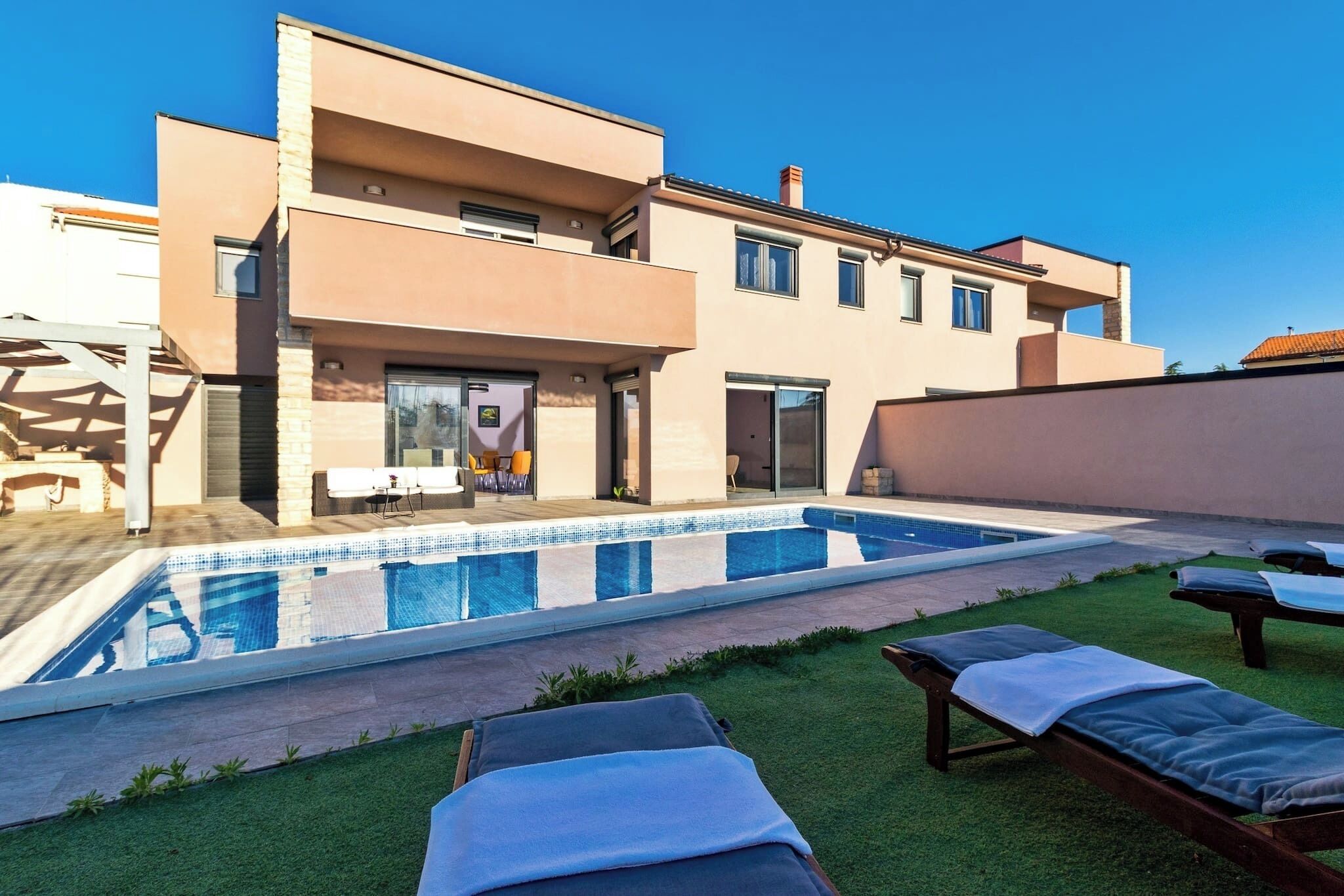 A modern two-story house with a swimming pool, outdoor lounge chairs, and a well-maintained lawn.