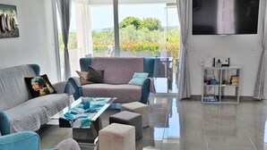 Een moderne woonkamer met een grote flatscreen-tv, een zithoek, een salontafel en een tv-meubel met elektronische apparaten.