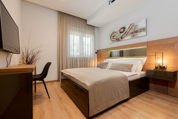 A modern hotel room with a bed, a desk, a chair, and a TV.