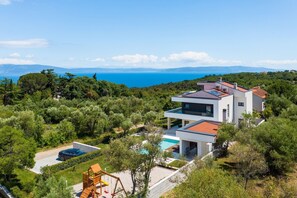 Una casa moderna de dos pisos con piscina, rodeada de exuberante vegetación y vista al mar.