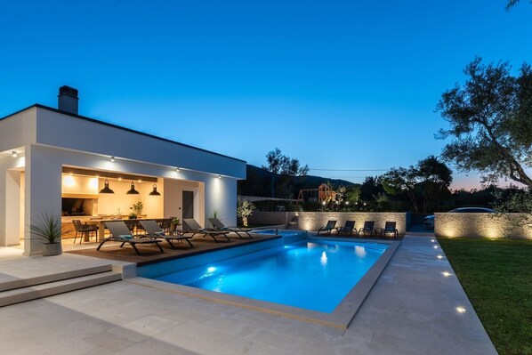 Una casa moderna con piscina, mobiliario de exterior y un patio bien iluminado.