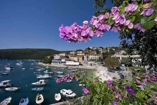 A coastal town with boats docked along the waterfront, buildings with balconies, and a clear blue sky.