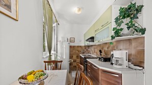 A kitchen with a dining table, chairs, a fruit bowl, a coffee maker, and cabinets. - Apartment Neda with Magnificent sea View (Rabac)
