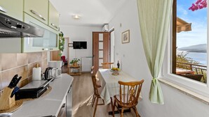 A compact kitchen with a dining area, a TV mounted on the wall, and a view of the sea through a window. - Apartment Neda with Magnificent sea View (Rabac)